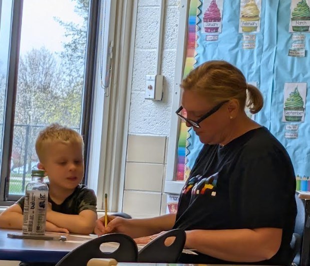 A female teacher and a little boy sitting at a table together working.