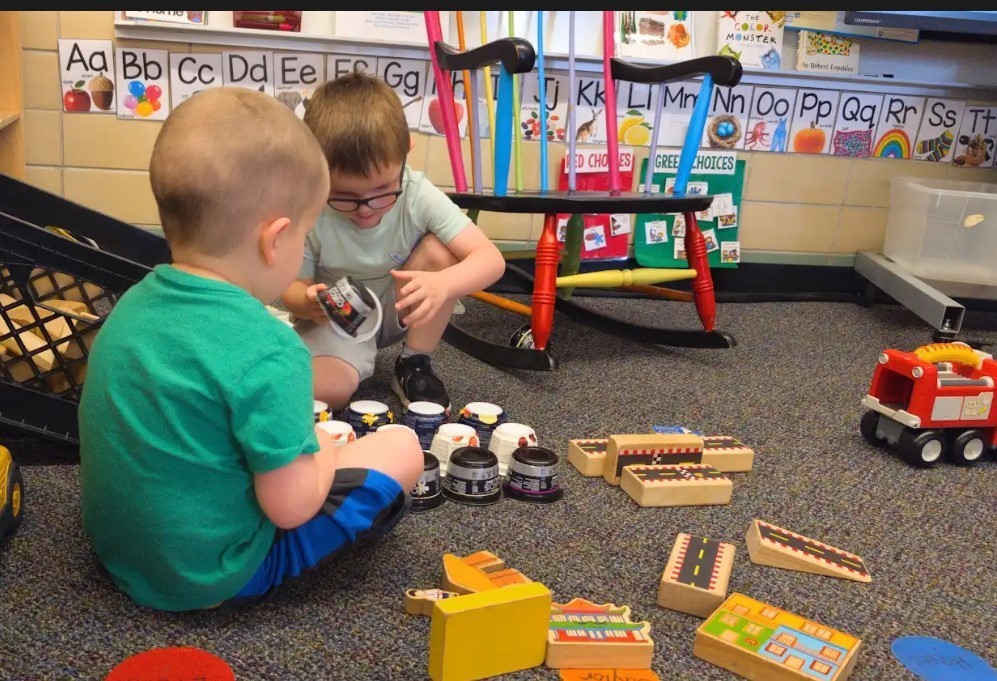 Two four year old boys lining up recylced yogurt cups on the carpet together.