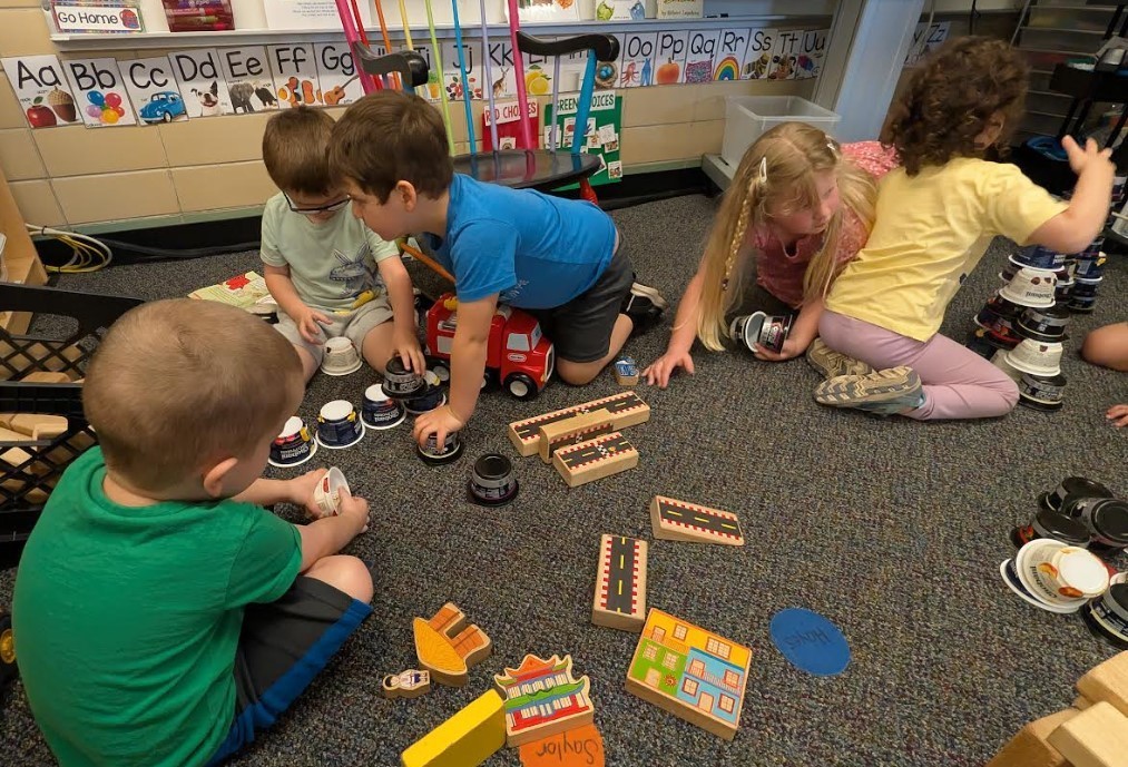 Multiple four year olds on the rug stacking cups and wooden blocks together.