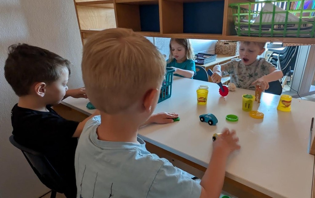 Four male students sitting at table together with cars and play-dough.