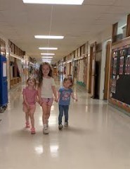 A first grade girl walking two girls down the hall together.