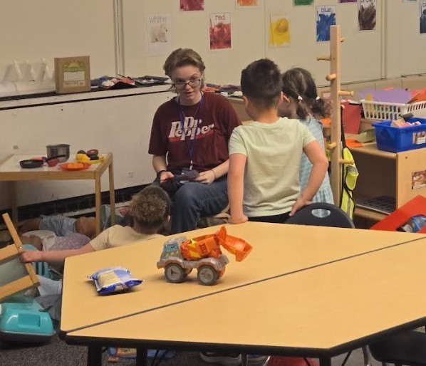 A teenager playing with preschool students in the play area.