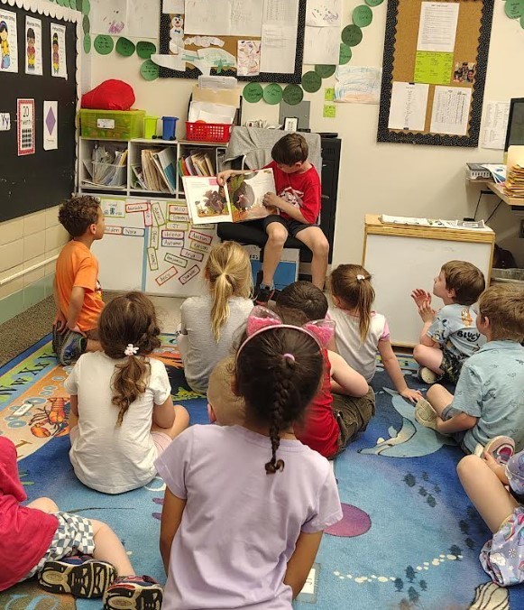 A child reading a book to a group of four year olds. 