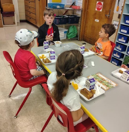 A 9 year old boy sitting with three four year old students at lunch.