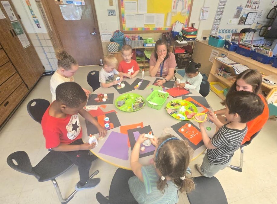 A teacher and 6 four year old students doing artwork together. 