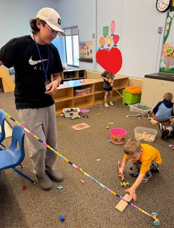 A tall teenage boy holding stacking cubes with a four year old. 