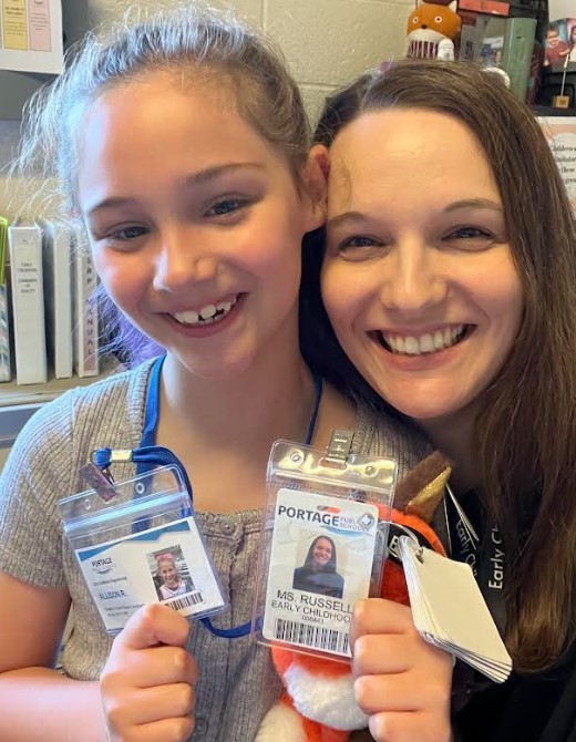 Two ladies smiling and holding their ID badges together. 