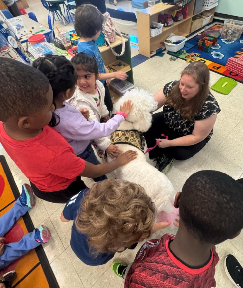 Students petting a white colored therapy dog together. 