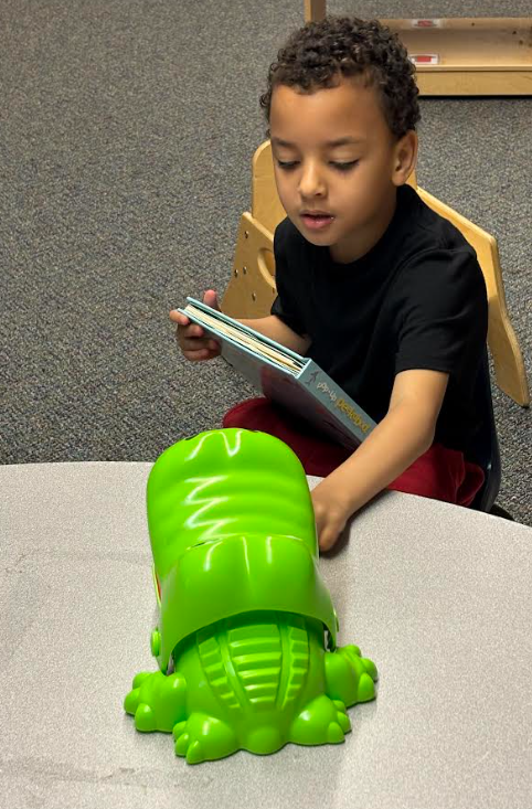 A little boy playing with a green alligator.