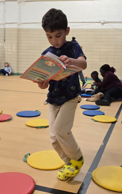 A little boy reading a book while standing.