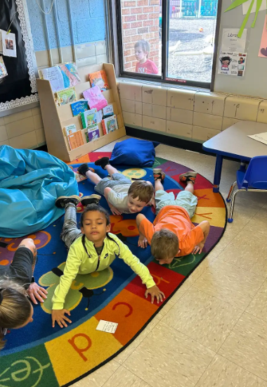 Three preschool boys laying on their stomachs on a floor trying to do yoga poses.