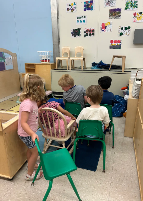 Four preschool students creating a pretend plane with chairs.