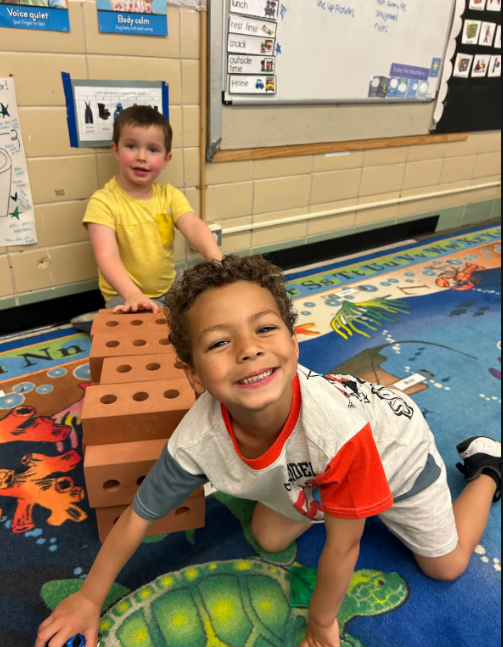 Two boys looking at the camera and smiling while they build blocks together. 