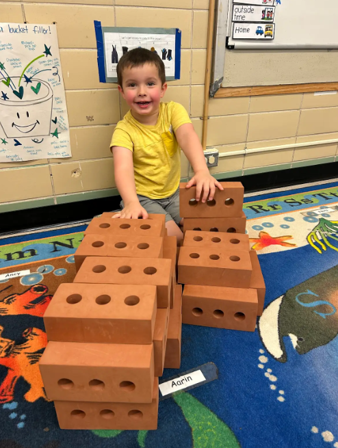 Two boys looking at the camera and smiling while they build blocks together. 
