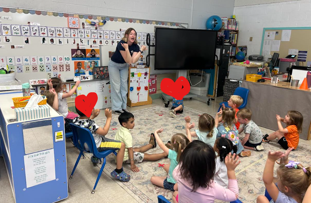 A teacher clapping and students following her lead. 