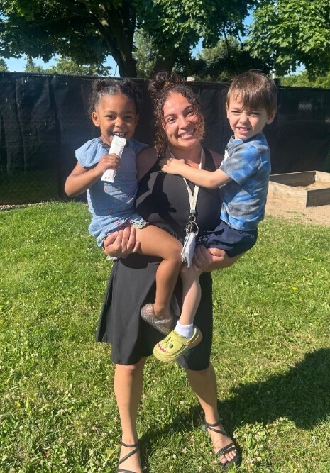 A teacher holding two preschool students in her arms. 