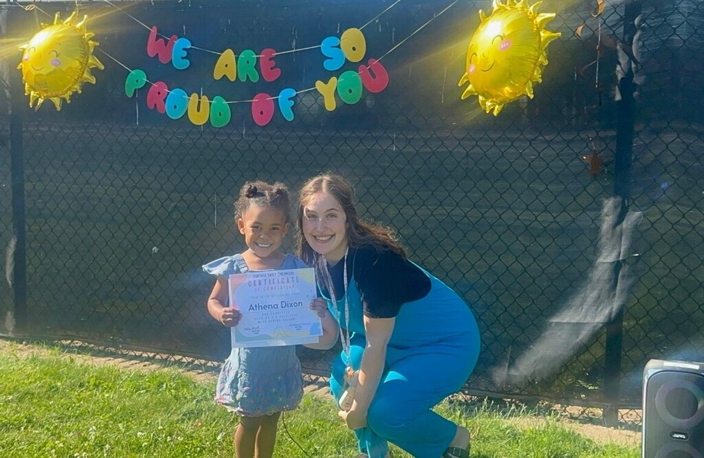 A teacher and a little girl holding a certificate and smiling. 