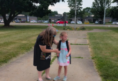 A female teacher and a little girl standing outside together.
