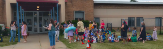 A group of teachers and students all outside the school waiting for their parents to arrive.