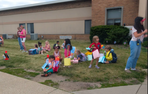A group of four year old students sitting on the lawn outside their school.