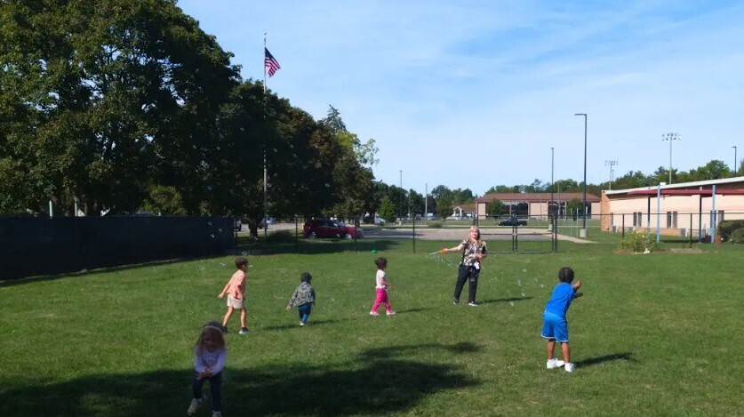 Students standing on the grassy field trying to catch bubbles in the air together.