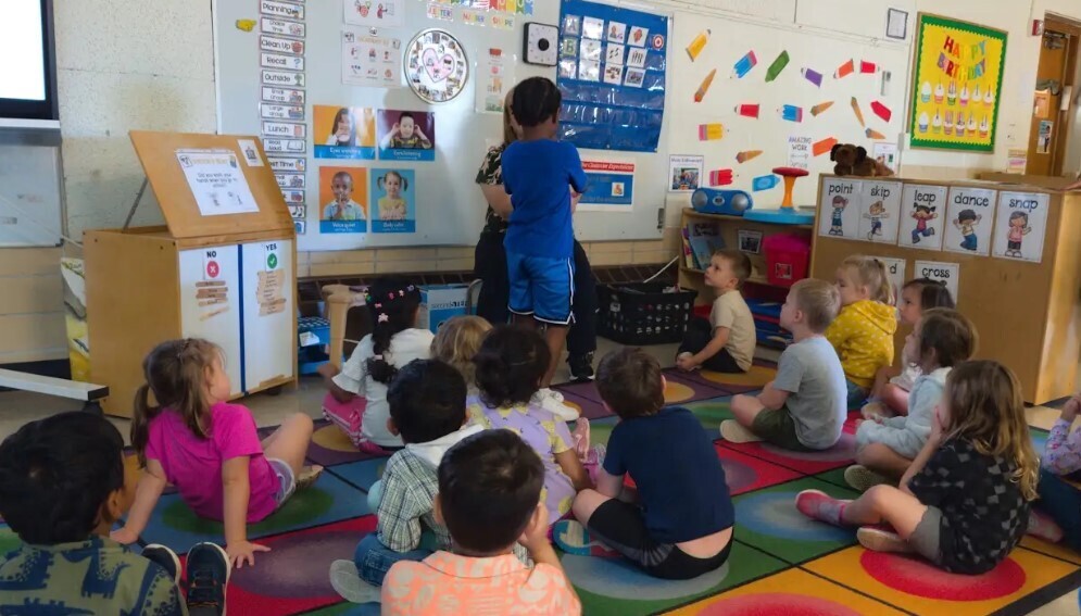 Four year old students sitting at the carpet together with their teacher.