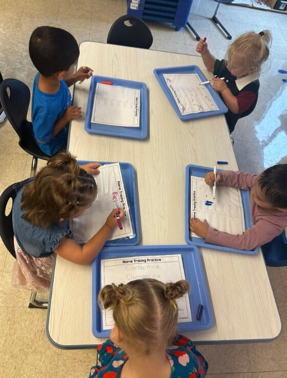 Students sitting at a table together and writting with a large marker.