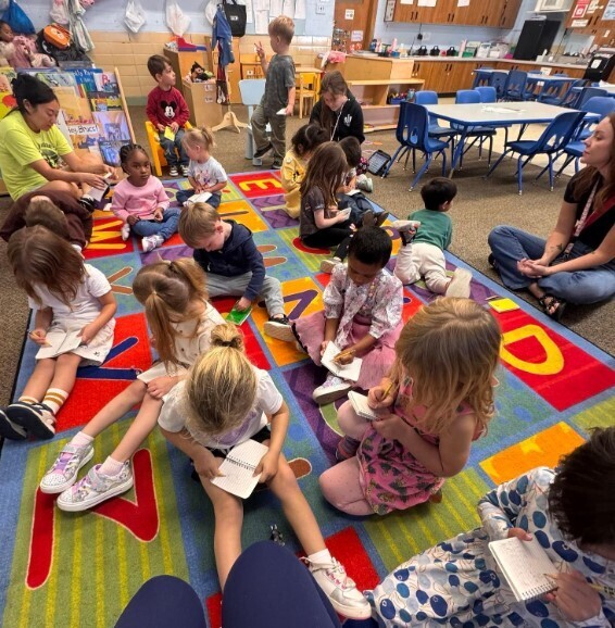 Students writting in journals on the carpet together.
