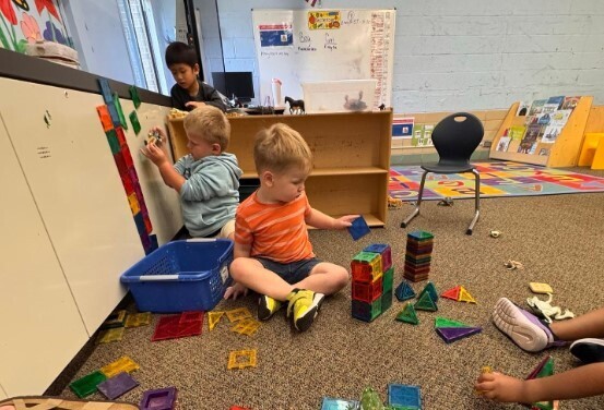 Three male students playing with magnetic blocks on the carpet together in the classroom.