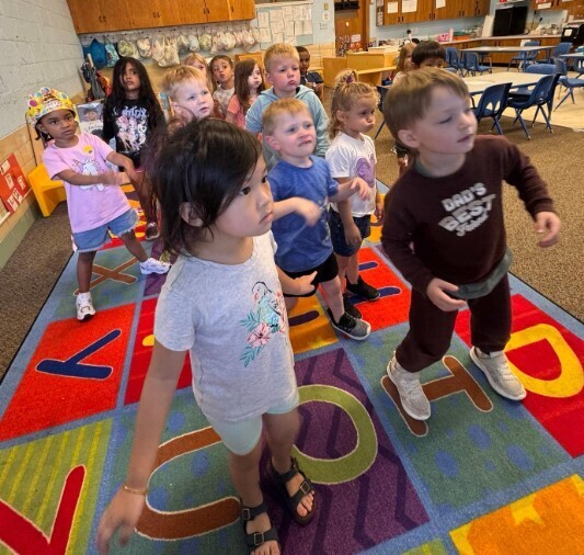 Preschool age students dancing together on their classroom rug.