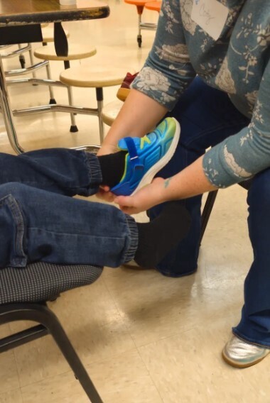 A little boy getting help putting on a new shoe.