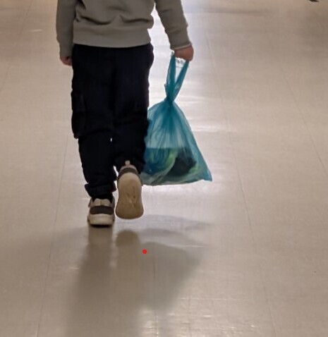 A little boy walking down the hall to class with his shoe bag.