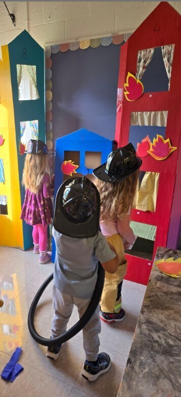 Two students making a fire with a fire hose in pretend play.