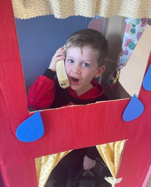 A little boy in the pretend firehouse holding a play phone.