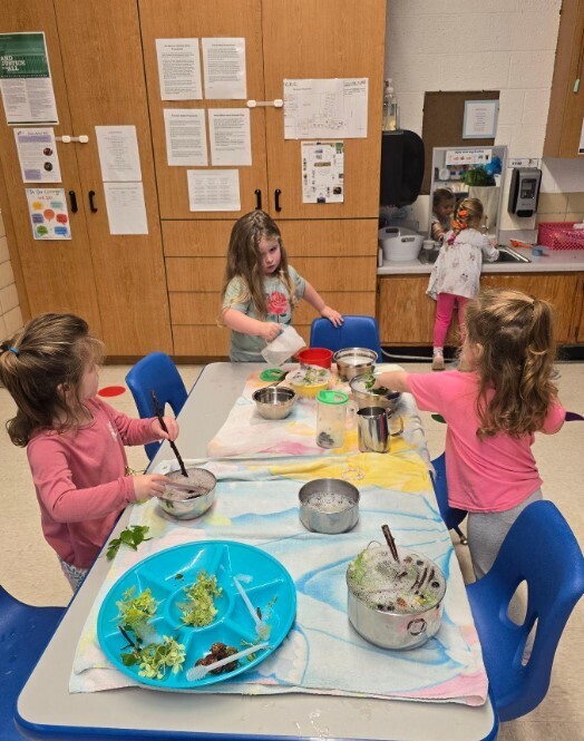 Three preschool girls making a potion together at a table.