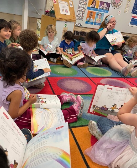 A group of students sitting at the carpet together holding music books and signing.