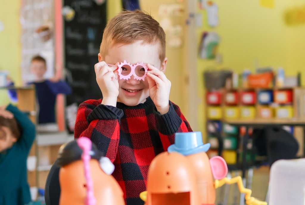 a young boy holds up glasses to his face