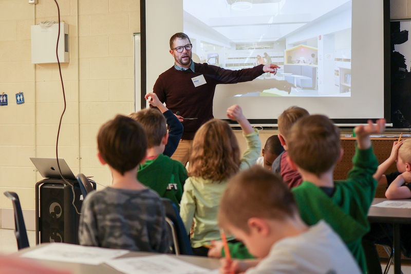 a man talking to students in front of a presentation