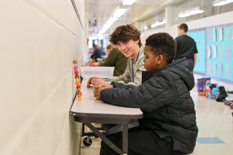 a high school boy sitting with another boy in a school hallway