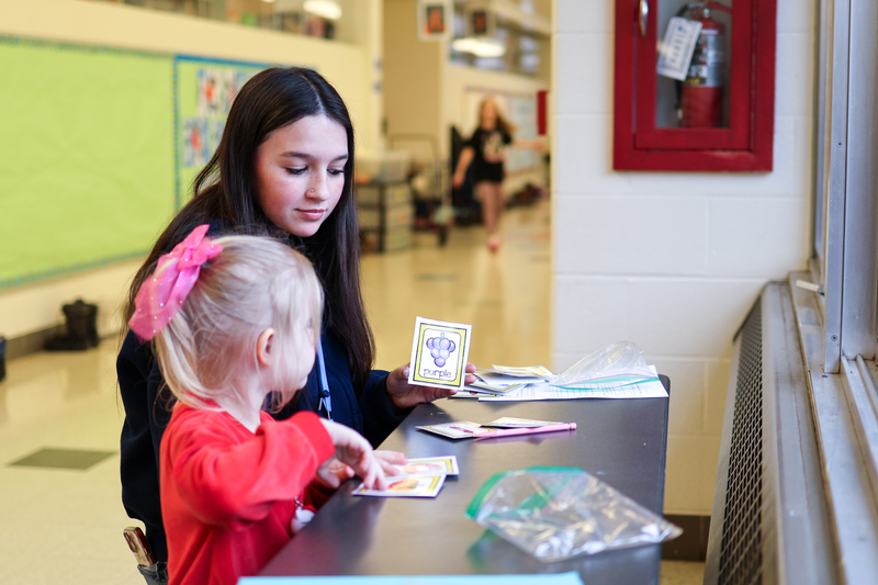 a high school girl sitting with an elementary student at a desk