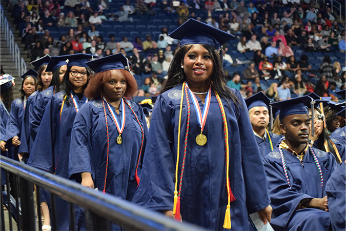 Student leading a line of graduates as they approach the stage