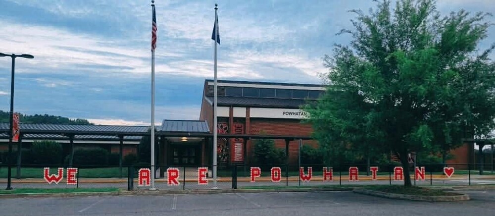 Exterior of Powhatan Elementary School with American and Virginia flags and a fence display spelling “WE ARE POWHATAN” with a heart.