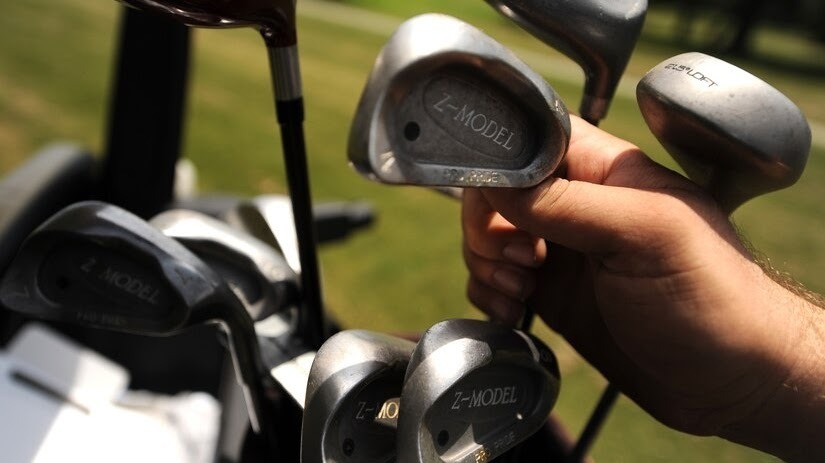 golf clubs with grass in the background and a hand holding one of the clubs.