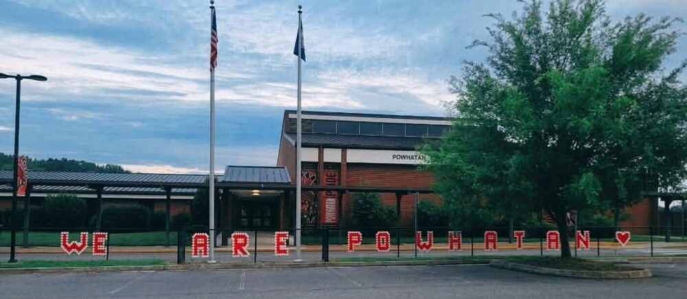 Exterior of Powhatan Elementary School with American and Virginia flags and a fence display spelling “WE ARE POWHATAN” with a heart.