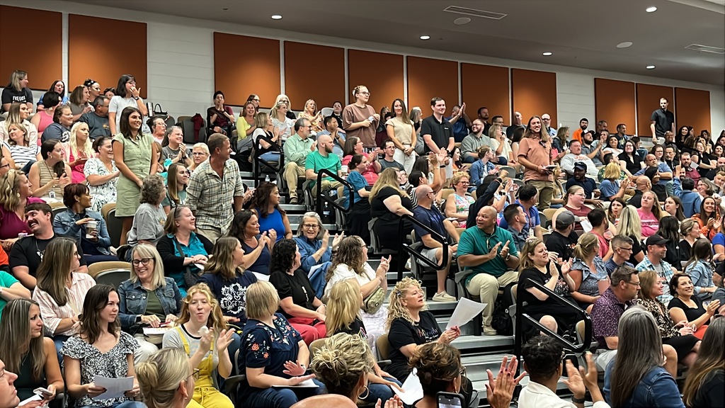 A large crowd of people sit in an auditorium clapping for some of them who are standing up.
