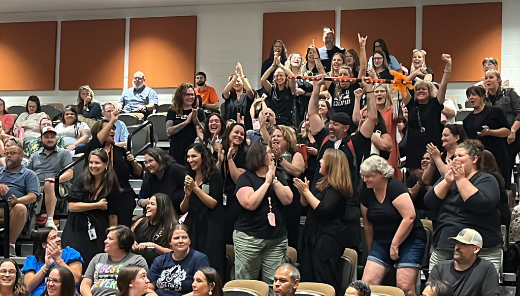 In the midst of a large crowd of people, a group stands cheering after winning the spirit stick. 