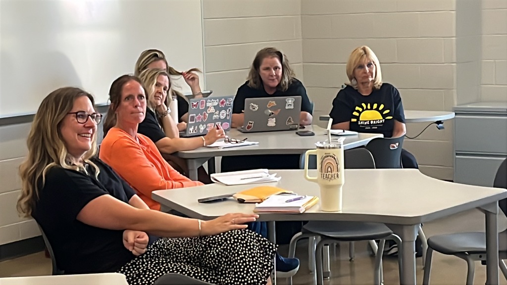 Staff members sitting at tables listen to a speaker during a professional development seminar. 