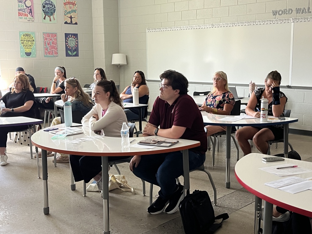 Staff members sitting at tables listen to a speaker during a professional development seminar. 
