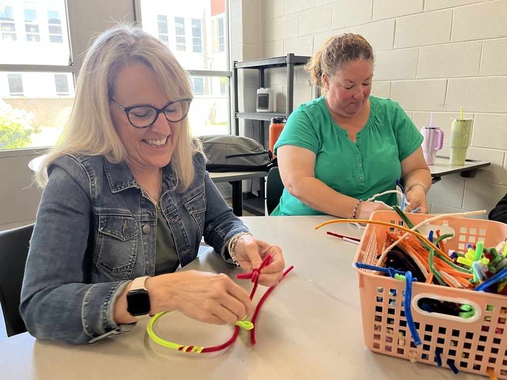 Two women sit at a table making a craft. 