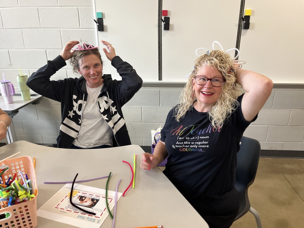 Two women sit at a table making a craft. 